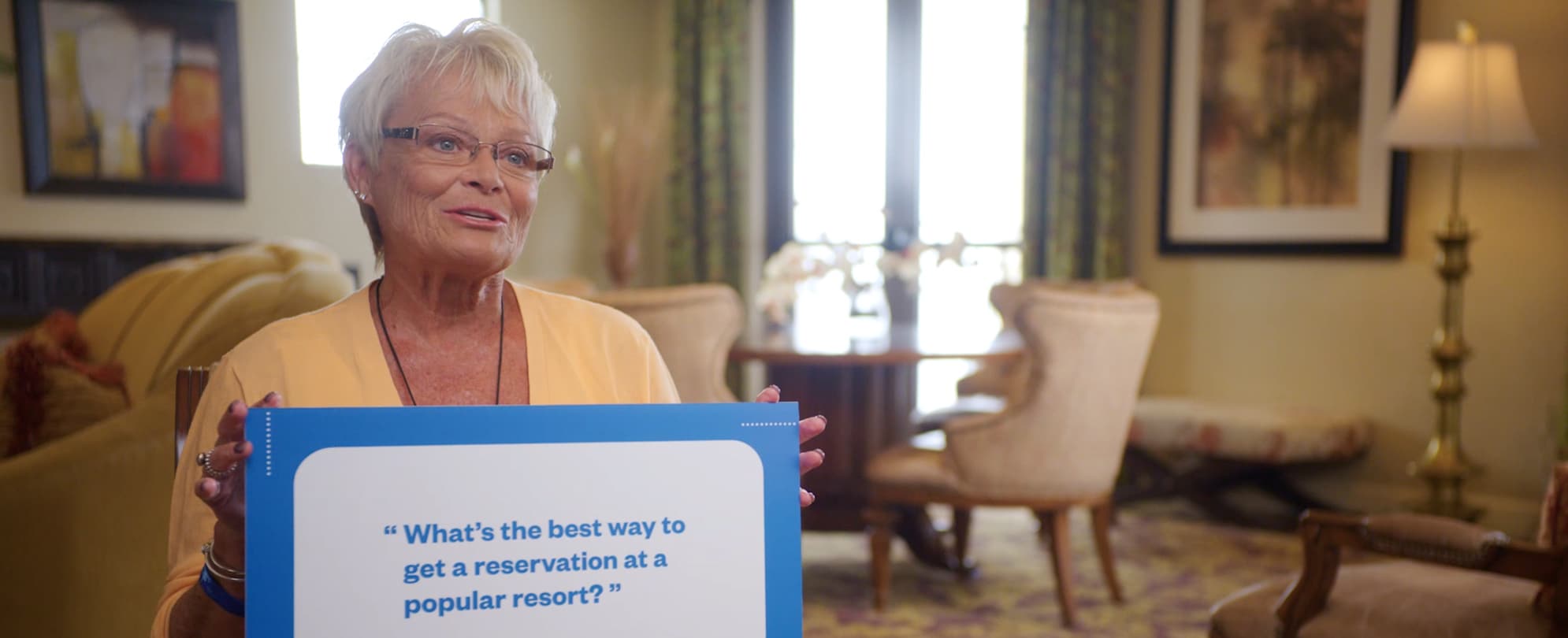An older woman holding a sign that says “What’s the best way to get a reservation at a popular resort?” 