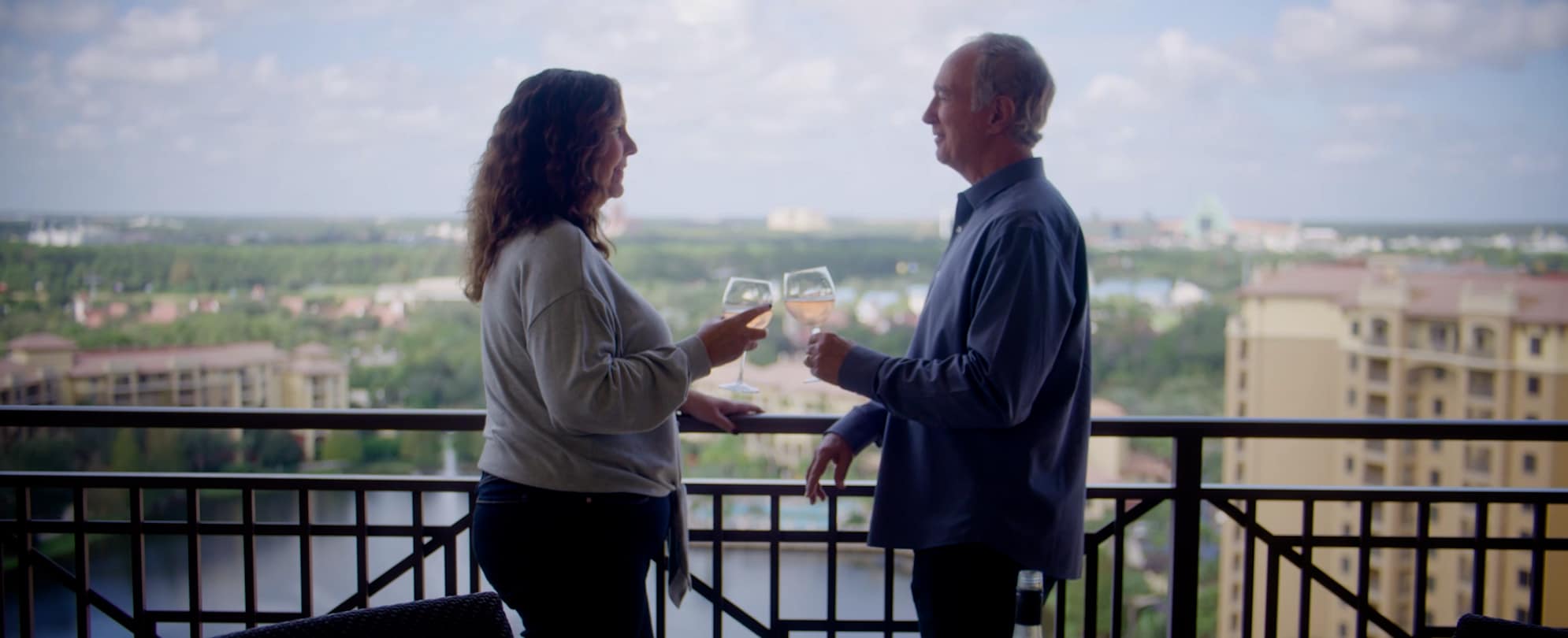 An older couple standing on a Club Wyndham resort balcony toasting with a glass of wine. 