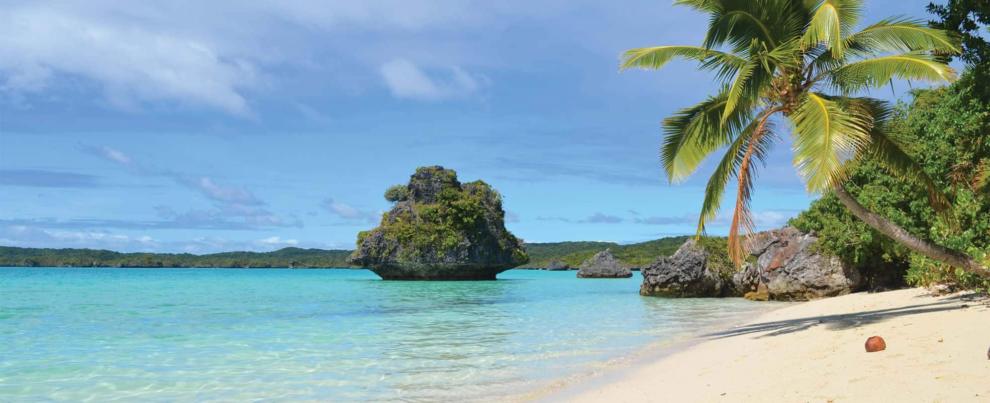 A tropical beach with turquoise water, rock formations, and palm trees.